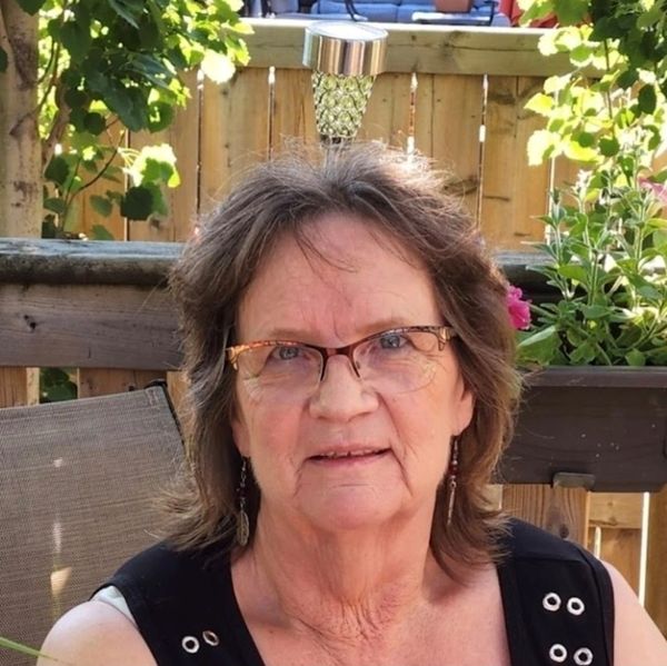 Smiling older woman with glasses sitting outdoors on a sunny day.