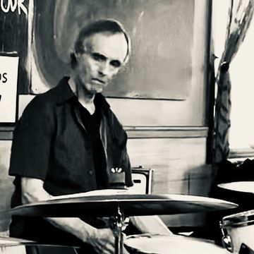 Black and white photo of a man playing drums in a room.