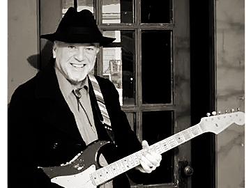 A man in a hat playing an electric guitar indoors.