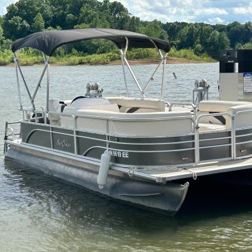 A pontoon boat with a canopy docked on a lake.