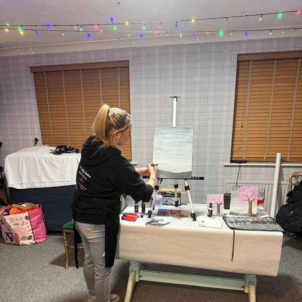 A woman painting on a canvas in a cozy room decorated with string lights.