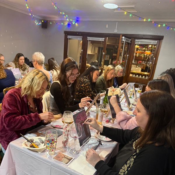 Women painting on canvases at a festive indoor art class with drinks and decorations.