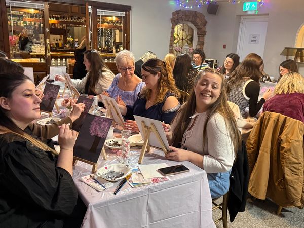 Group of women enjoying a guided painting session in a cozy, decorated room.