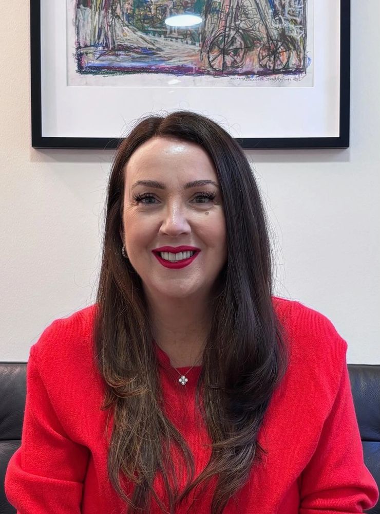 Smiling woman with long dark hair wearing a red sweater and red lipstick.
