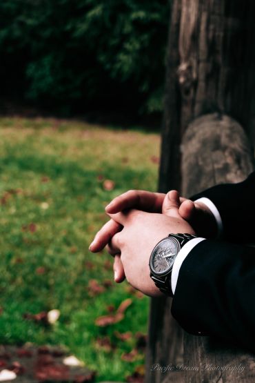 Close-up of hands with a wristwatch resting on a wooden surface outdoors.