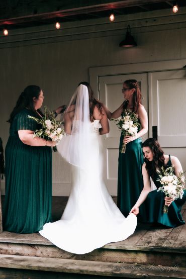 Bride with bridesmaids in green dresses adjusting her wedding gown.