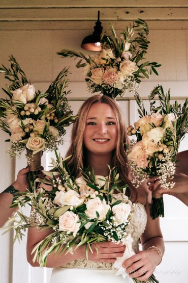 Bride holding multiple bouquets of white and cream flowers with greenery.