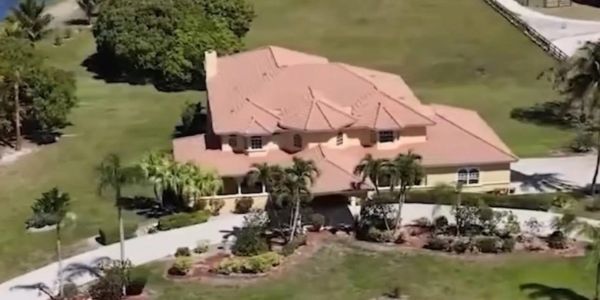 Large house with red roof and surrounding greenery.