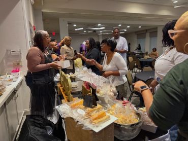 People interacting at a busy indoor market stall with baked goods.