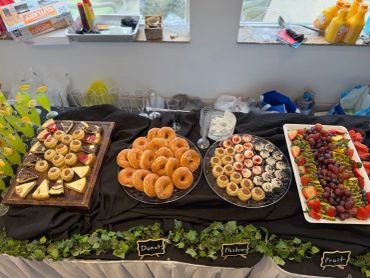 A table with donuts, pastries, and fresh fruit arranged for a buffet.