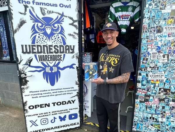 A man stands smiling outside Wednesday Warehouse, holding a magazine.