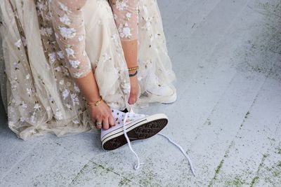 A woman in a floral white dress putting on a pair of white sneakers