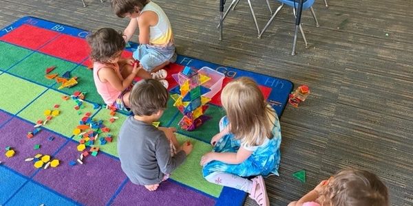 Children playing with colorful building tiles on a multicolored carpet.