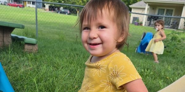 Toddler smiling outdoors near a fence.