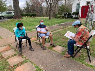 Two children sitting outdoors with an adult reading to them.