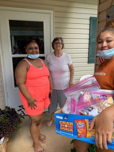 Three women standing outside a porch with snacks.