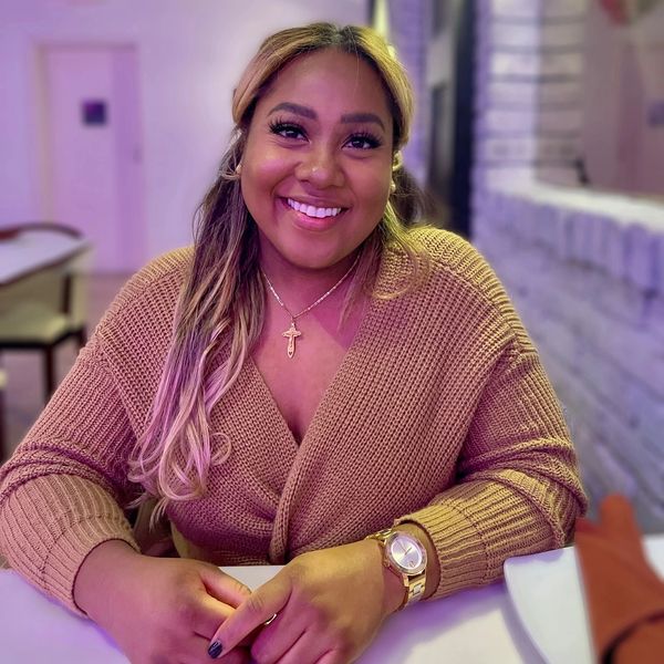 Smiling woman in a cozy brown sweater sitting at a table indoors.