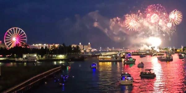 Fireworks over a river with boats and a ferris wheel at night.