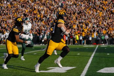 Iowa football players running on the field during a game with a large crowd in the background.