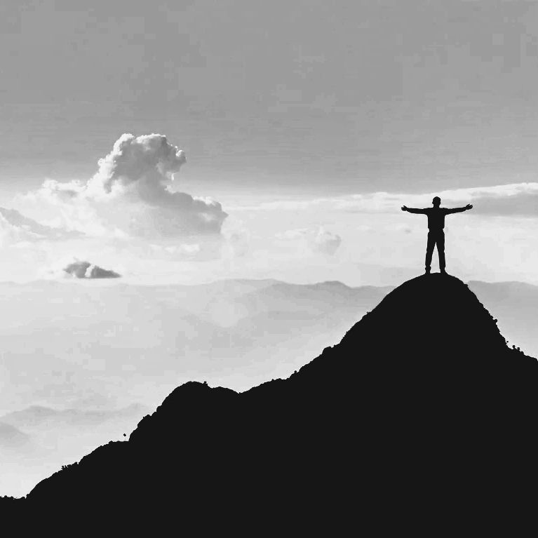 Silhouette of a person standing triumphantly on a mountain peak with arms outstretched.