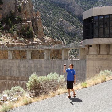 A man in blue shirt taking photo near a large dam in a mountainous area.