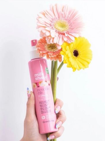 Hand holding pink spray bottle and colorful flowers.