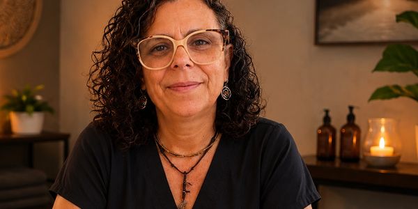 Woman with curly hair and glasses smiling warmly indoors.