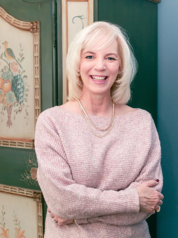 Smiling woman with blonde hair wearing a pink sweater and gold necklace.