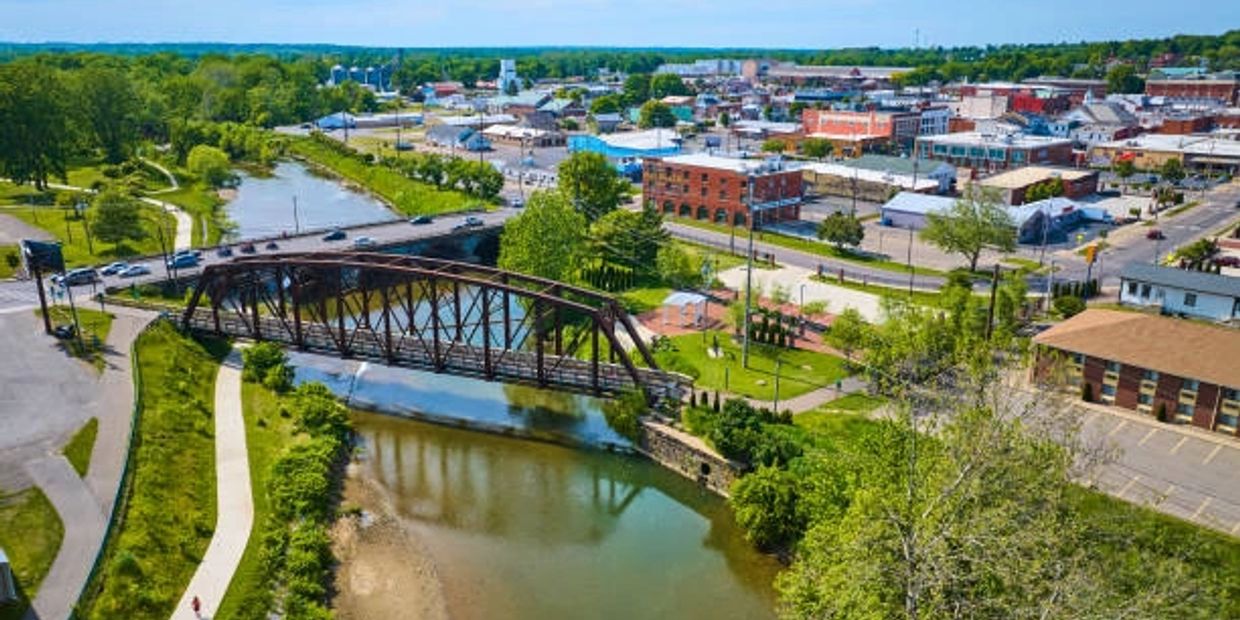 A bridge over a river in a small town with greenery and buildings.