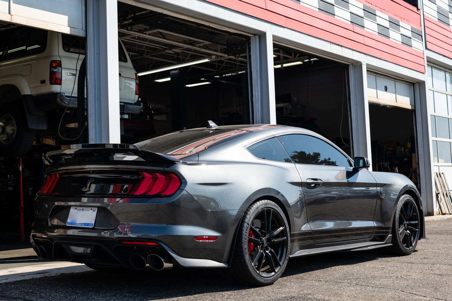 grey Mustang parked in front of open garage doors of maintenance shop