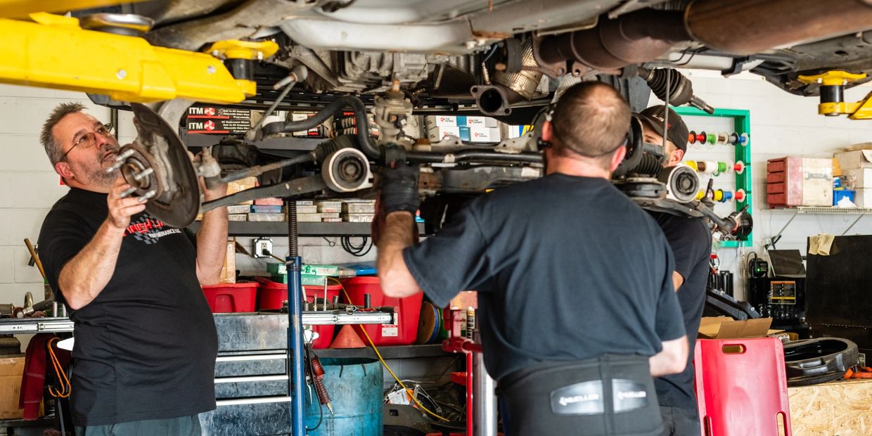 Three men wearing Finish Line uniform performing work on car