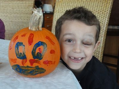 A smiling boy with a painted pumpkin on a table.