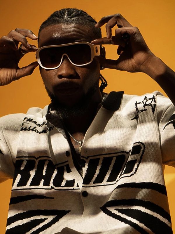 Man adjusting stylish white sunglasses against a warm orange background.