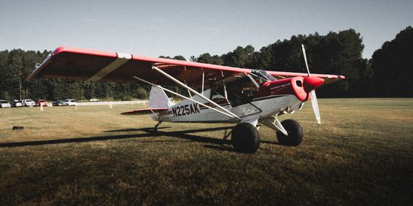 Small red and white single-engine airplane on grass field.