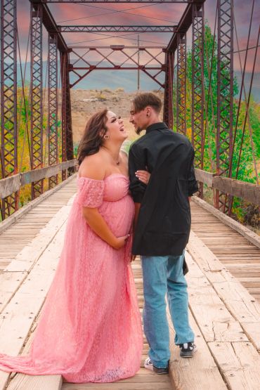 Pregnant woman and partner on a rustic bridge.
