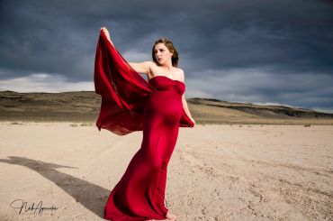 Pregnant woman in a flowing red dress on a desert landscape.