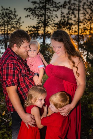 Family photo with a pregnant mother, father, and three children outdoors.