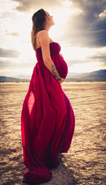 Pregnant woman in a flowing red dress standing in a barren landscape.