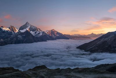 Snow-capped mountains at sunset above a thick sea of clouds.