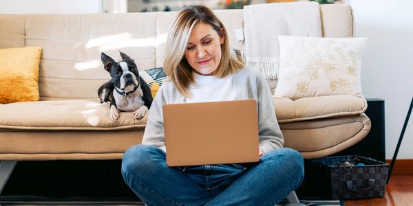 Blonde woman sitting cross-legged on the floor typing on a lap-top.