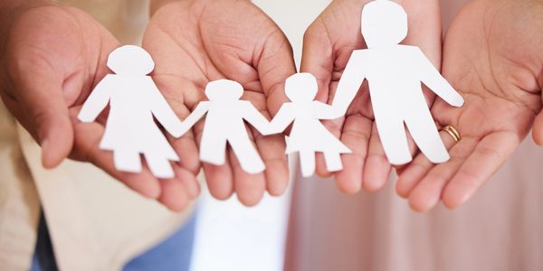 Two people with palms outstretched holding a chain of paper dolls that represent a family.