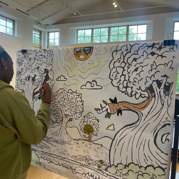 An artist paints a large whimsical tree mural indoors.