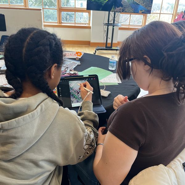 Two students collaborating on a digital art project using a tablet.