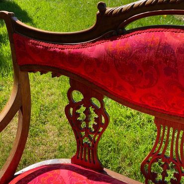 Ornate wooden chair with red upholstery on a green lawn.