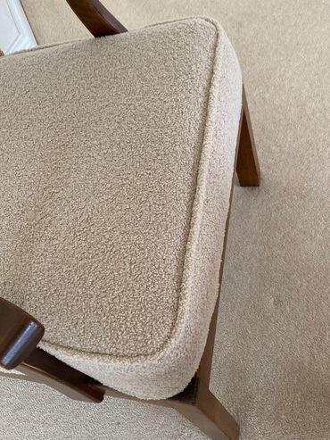 Close-up of a beige cushioned chair with wooden frame on carpeted floor.
