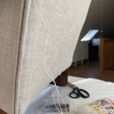 Loose white threads hanging from beige upholstered furniture.