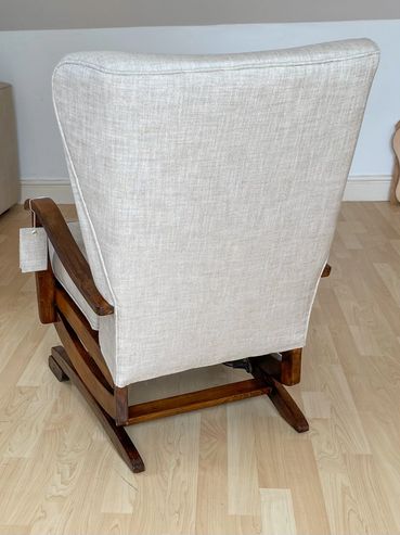 Beige upholstered rocking chair with wooden frame on light wood floor.