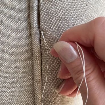 Hand sewing a beige fabric with a needle and thread.