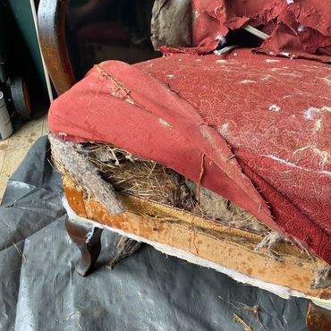 Old, torn red armchair showing internal stuffing.