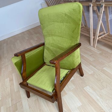 Green cushioned wooden chair with missing seat cushion in a room.